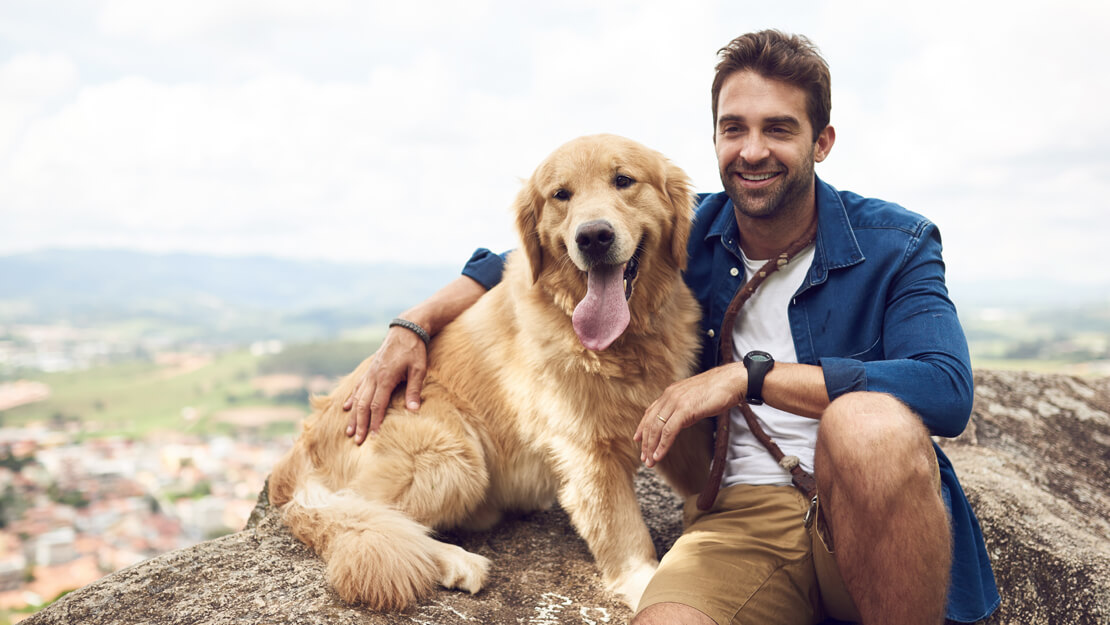 young man sitting on a hill with his golden retriever