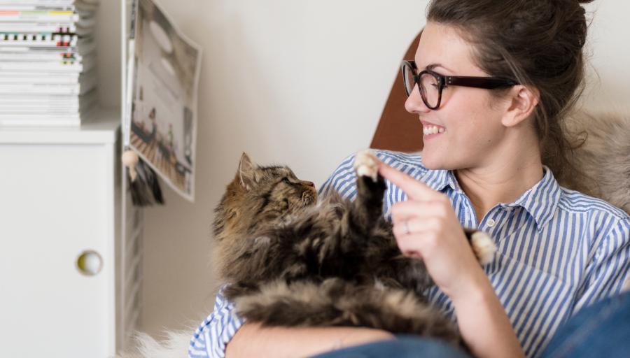 Une femme assise avec son chat sur les genoux touche la patte de celui-ci avec son doigt.