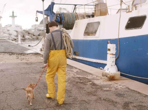 pêcheur promenant son chien à côté d'un bateau de pêche