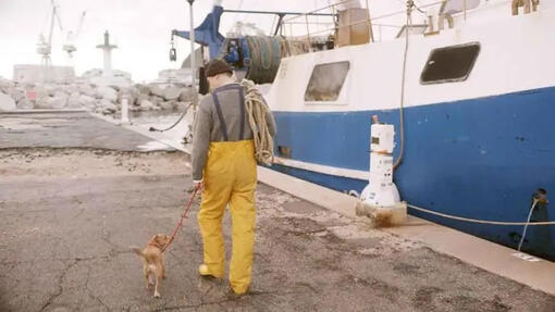 visser laat zijn hond uit naast een vissersboot
